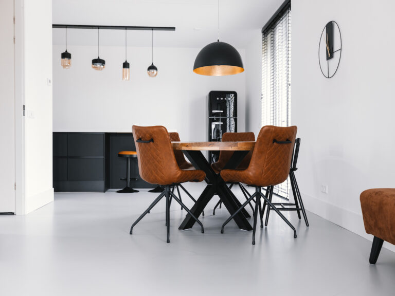 Lichtgrijze gietvloer in een eetkamer met zwarte keuken