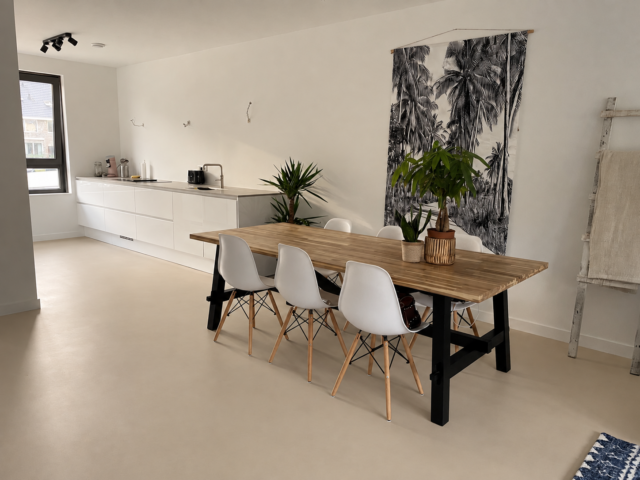 Beige gietvloer in een woonkeuken met houten eettafel